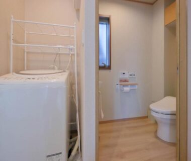 Washing machine and rack beside toilet in compact ryokan unit at Kyo Machiya Ryokan Yuan Kyoto