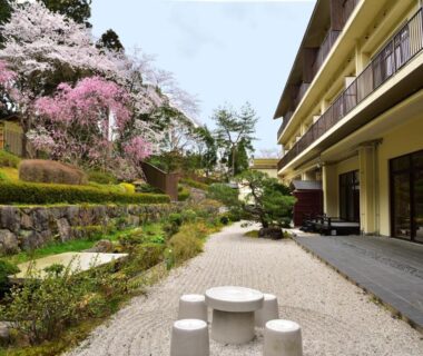Courtyard with stone seating, gravel terrace, flowering cherry trees and ryokan balconies at Kyo Yunohana Resort Suisen Kyoto