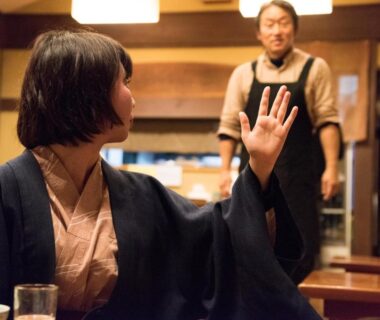 Guest in traditional attire raising hand in ryokan dining room with staff visible, Kyo no Minshuku Ohara no Sato Kyoto