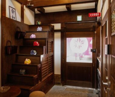 Genkan with wooden shelving and decorative pouches on steps, shoji door and stone floor at Kyomachiya Bettei Hanatei Kyoto
