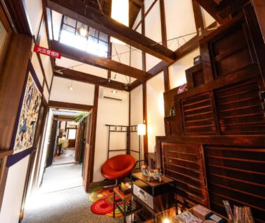 Interior corridor with exposed wooden beams, sliding wooden doors and seating at Kyomachiya Bettei Hanatei in Kyoto