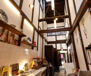 Interior corridor with high wooden beams, display shelves and pendant lights at Kyomachiya Bettei Hanatei Kyoto