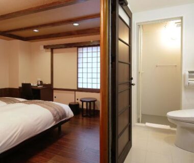 Wood floor room with bed, shoji screen window and en suite bathroom at Kyomachiya Ryokan Sakura Urushitei Kyoto