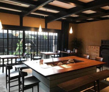 Communal dining room with central wooden counter, low stools and shoji-style windows in Kyoto ryokan