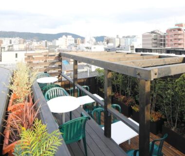 Rooftop terrace seating with pergola, small tables and city view at Kyomachiya Ryokan Sakura Urushitei, Kyoto