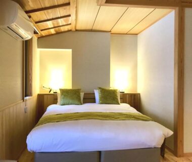 Double bed with green cushions, wooden ceiling and warm lighting in Kyomachiya Ryokan Sakura Urushitei room, Kyoto, Kansai