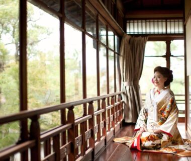 Woman in kimono seated on wooden engawa with shoji screens overlooking a lush ryokan garden