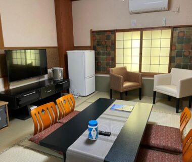 Tatami room with low table, zabuton chairs, shoji screens, TV, refrigerator and lounge chairs at Kyoto Ryokan Gion Sano