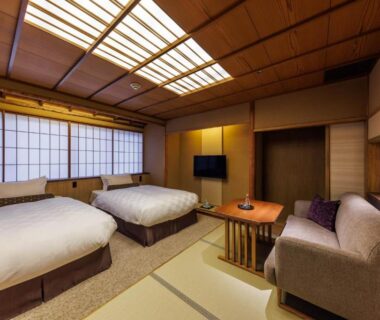 Traditional tatami room with twin beds, shoji screens, low table, sofa, and wooden ceiling at Kyoto Ryokan SAKANOUE