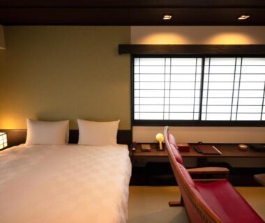 Bright ryokan room with white bed, shoji screens, wooden desk and red armchair, tatami flooring and soft ambient lighting
