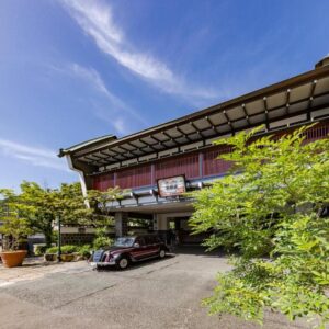 Covered ryokan entrance with vintage car, wooden facade and greenery under a bright blue sky at Kyotoya in Saga, Kyushu