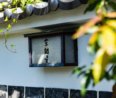 Wooden framed sign with Japanese characters on a plaster wall at Kyotoya in Saga, Kyūshū with blurred foliage