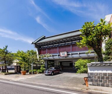 Two-story wooden ryokan entrance with tiled wall, potted plants and street view in Saga, Kyūshū, Japan