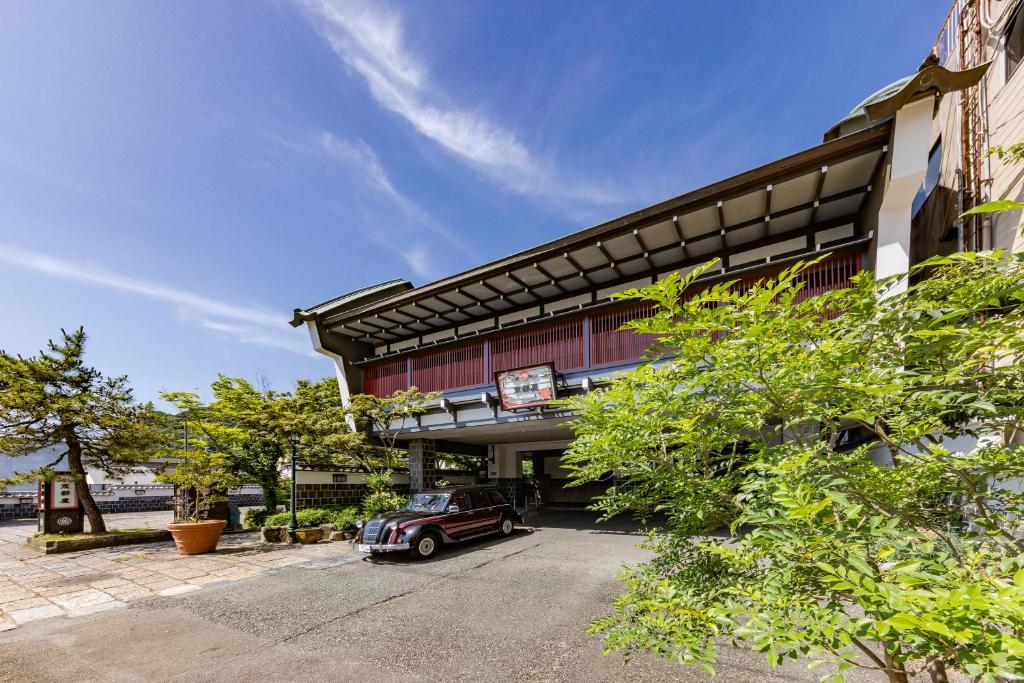 Entrance driveway with vintage car Kyotoya Saga Covered ryokan entrance with vintage car, wooden facade and greenery under a bright blue sky at Kyotoya in Saga, Kyushu
