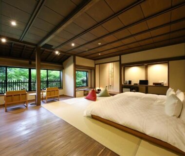 Spacious tatami room with low beds, wooden floors, shoji screens and balcony overlooking greenery