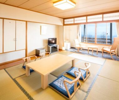 Spacious tatami room with low table, floor cushions, TV and window seating at Kyukamura Iwate-Amiharionsen, Iwate