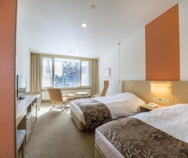 Bright twin room with seating area and desk at Kyukamura Nikko-Yumoto in Tochigi, Kantō, Japan