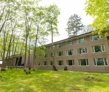 Low-rise ryokan building on grassy lawn with surrounding green trees, Kyukamura Nikko-Yumoto in Kantō, Tochigi, Japan