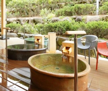 Wooden deck with round soaking tubs, water spouts and chairs by terraced garden at Kyukamura Noto-Chirihama, Ishikawa, Japan