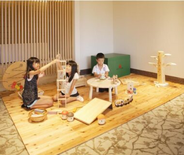 Children playing on wooden play mat with low table and toys at Kyukamura Noto-Chirihama in Ishikawa