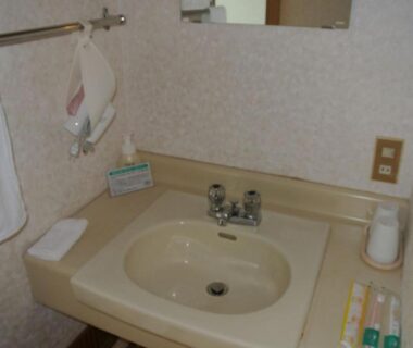 Beige vanity sink with mirror, towels and toiletries at Kyukamura Ohkunoshima in Hiroshima