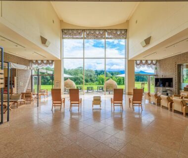 Bright lounge with floor-to-ceiling windows and seating facing garden and hills at Kyukamura Ura-Bandai Fukushima Tōhoku