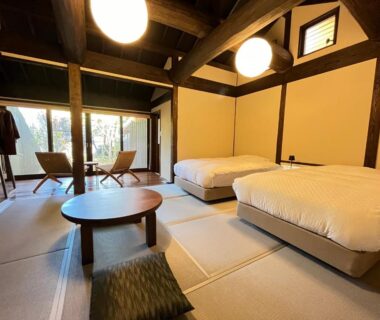 Tatami room with twin low beds, round table, wooden beams and balcony seating at Kyutei in Kumamoto