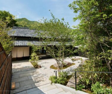 Stone pathway and courtyard leading to a traditional ryokan entrance with tiled roof and garden trees in Shizuoka