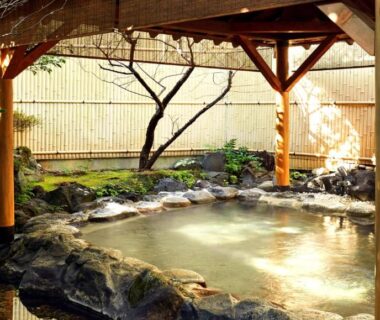 Sheltered outdoor onsen with stone bath, wooden posts and bamboo fence at Laforet Ito Onsen Yunoniwa, Shizuoka