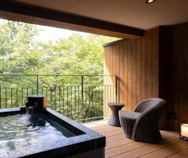Wooden outdoor onsen bath on deck with chairs and leafy mountain view at Laforet Shuzenji Sanshisuimei Shizuoka