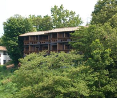 Three-story wooden ryokan with balconies nestled in green hillside at Laforet Shuzenji Sanshisuimei, Shizuoka