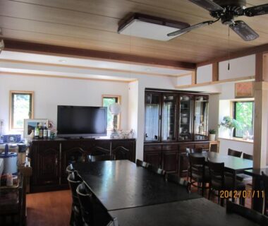 Wood-paneled dining area with long tables, chairs, ceiling fan and cabinet at Lake Oshino, Yamanashi