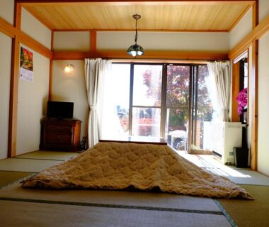 Tatami room with futon on mats, sliding glass doors, wooden ceiling, small TV cabinet and balcony view