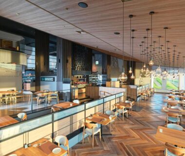 Spacious wooden dining area with pendant lights, tables and large windows overlooking outdoor greenery