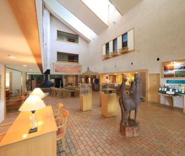 Sunlit atrium lobby with seating, wooden sculpture and reception area at Lake Saroma Tsuruga Resort Hokkaidō