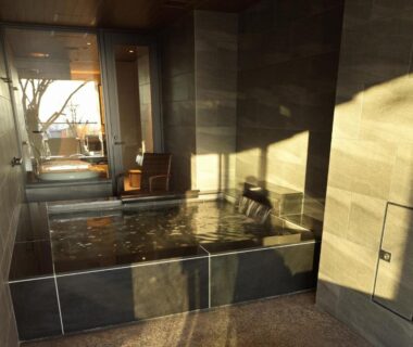 Indoor stone bath with wooden seating and sunlight at Lake Shikotsu Tsuruga Bessou AO no ZA Hokkaidō