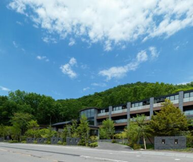 Low-rise ryokan building with balconies set against a green hillside near Lake Shikotsu, Hokkaidō