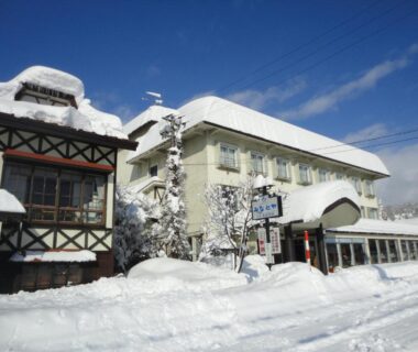 Snow-covered ryokan exterior with deep snowbanks and clear blue sky in Fukushima, Tōhoku