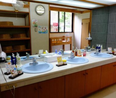 Communal vanity with three sinks, mirrors, toiletries and wooden cabinetry at Lake Yamanakako Shuzansou in Yamanashi