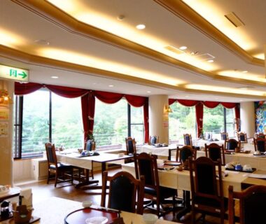Ryokan dining room with wooden tables, chairs and large windows overlooking greenery at Lake Yamanakako Shuzansou Yamanashi