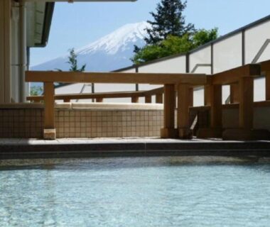 Outdoor onsen bath with tiled pool, wooden railings and Mount Fuji in the background