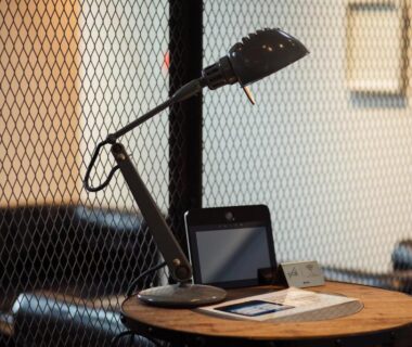 Adjustable desk lamp on wooden table with tablet and leather seat by metal mesh at Lampstand STAY Asahikawa Hokkaidō