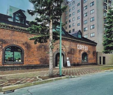 Brick coffeehouse facade with nearby hotel building at Lampstand STAY Asahikawa, Hokkaidō, Japan