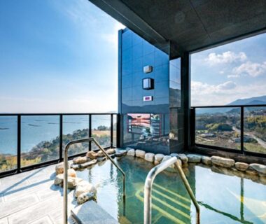 Rooftop stone onsen with glass railing and coastal view at LiVEMAX RESORT Aki Miyahama Onsen, Hiroshima