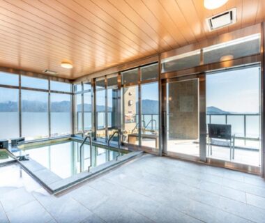 Indoor onsen bath with large windows overlooking bay and distant hills at LiVEMAX RESORT Aki Miyahama Onsen Hiroshima