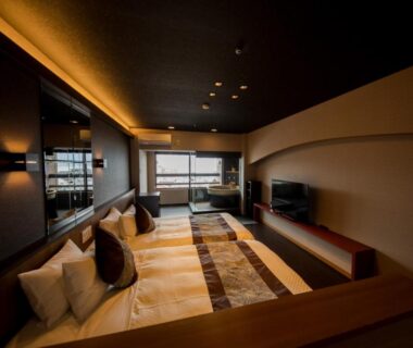 Warm-lit modern guest room with low beds, wooden accents and seating, large window at LiVEMAX RESORT Aki Miyajima