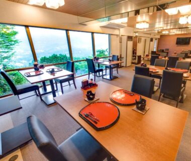Dining area with lacquer trays, tables, chairs and large windows overlooking greenery at LiVEMAX RESORT Hakone Sengokuhara