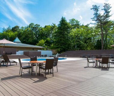 Sunlit outdoor pool deck with tables, chairs and umbrellas surrounded by trees at LiVEMAX RESORT Kaga Yamashiro, Ishikawa