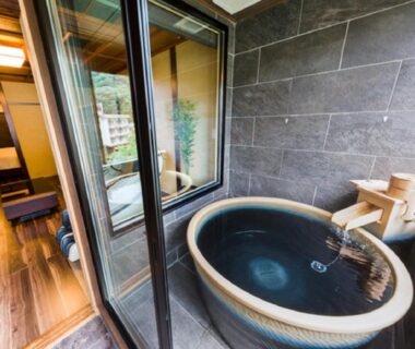 Round soaking tub on balcony with wooden spout and sliding glass door to guest room at LiVEMAX RESORT Kawaji