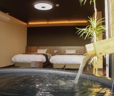 In-room wooden soaking tub with flowing spout, twin beds and warm lighting at LiVEMAX RESORT Kinugawa, Tochigi